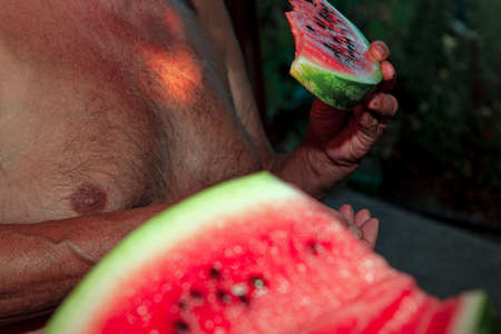 Old man holding sliced watermelon in hand . Man eating fresh watermelonの写真素材