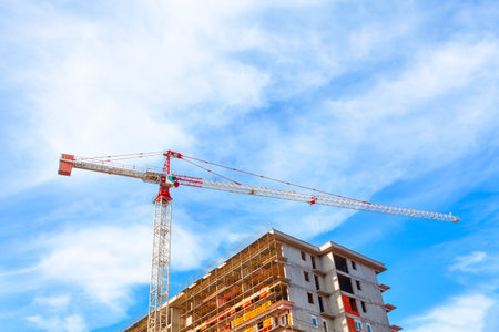 Crane and building under construction against blue sky with white clouds.の写真素材