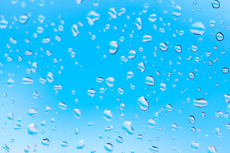 Macro shot of water droplets clinging to a glass surface . Water drops at window glass against blue skyの写真素材
