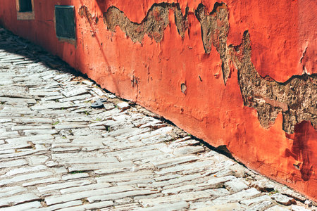 Old wall with plaster cracks and cobblestone road. Vibrant red wall with a contrasting pavement....