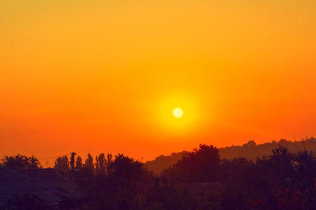 Sunset over rustic hillside with trees in foreground. Serene and picturesque landscapeの写真素材