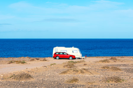 Car and camper parked on beach. Red car is parked next to a trailer on a beach. The scene is peaceful and serene, with the ocean in the background and the trailer providing a sense of relaxation and leisureの写真素材