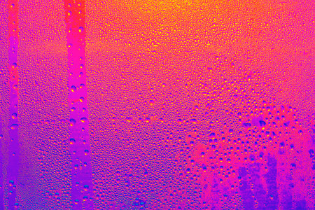 Colorful background with many small droplets of water. The background is a mix of pink, orange, and purple.  Raindrops on a window surfaceの写真素材