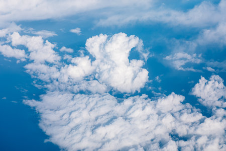 Serene view of the sky from an airplane with scattered white clouds above. The clouds are white and...