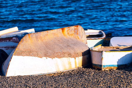 Fishing boats resting on the sandy beach, surrounded by gentle waves. Row of old boats are sitting...