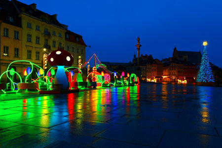 Festive nighttime scene in a city square, adorned with colorful holiday lights and decorations. Christmas tree with garlands and star on top, various reflections of the lights on the wet pavementの写真素材
