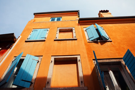 Facade of brightly colored orange building with blue wooden shutters, some are open and some closed. Contrast between vibrant orange walls and blue shutters creates aesthetically pleasing sceneの写真素材