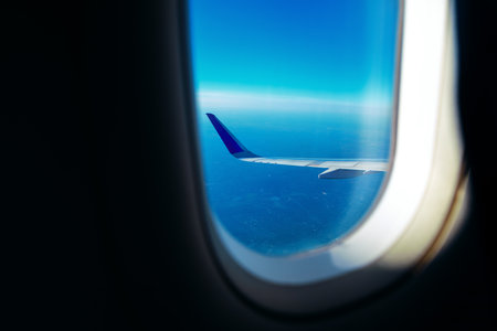 View from an airplane window showcasing a wing against a stunning blue sky and distant horizon, capturing the serene beauty and excitement of air travel at cruising altitudeの写真素材
