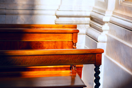 Wooden pews inside a church or chapel, sunlight casting shadows on the polished wood surfaces. Intricate design of the pews, including the twisted spindle supports and rich tones of the woodの写真素材