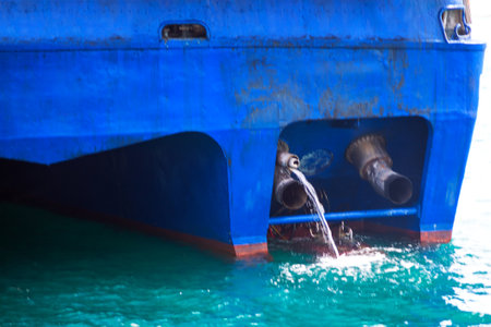 Stern of blue ship with water being discharged from two large pipes into the sea. Ship's bilge and ballast water being pumped out, which is a common operation in maritime activitiesの写真素材