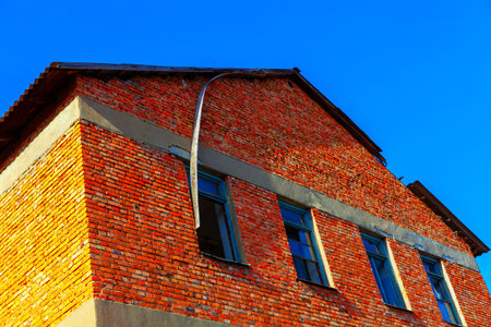 Red brick building with blue-framed windows under a clear blue sky. The structure shows rustic...