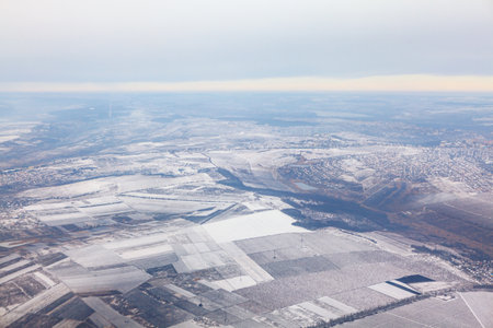 Aerial view of vast landscape covered in snow with patchwork of fields and village visible. Horizon...
