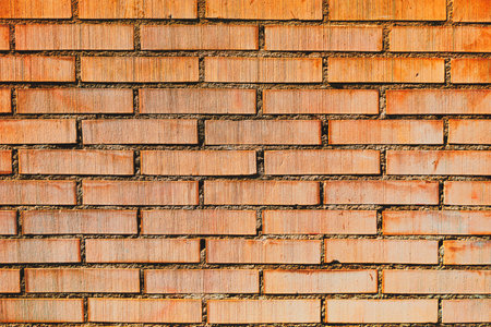 Textured brick wall with a consistent pattern of rectangular bricks arranged horizontally and vertically. The bricks are red light in color, with visible mortar joints between themの写真素材