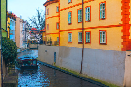 Picturesque scene of Certovka canal in Prague, with a boat navigating narrow waterway flanked by colorful buildings. Vibrant building along with serene water and boat create a charming atmosphereの写真素材