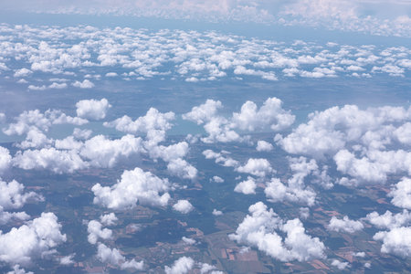 Bird's eye view of a landscape with a scattering of fluffy white clouds in the sky. Ground below features patches of land in various shades indicating fields and possibly forests or other vegetationの写真素材