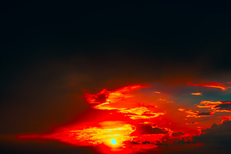 Mesmerizing sunset with sun descending near horizon, bathing sky in warm glow. Dramatic clouds painted in fiery shades of red, orange, create vivid and breathtaking contrast against deepening duskの写真素材