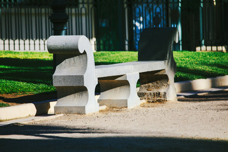 Weathered gray stone bench, nestled in a grassy park, casts long shadows in the afternoon sun. Ornate stone bench, a tranquil spot in a well-maintained parkの写真素材