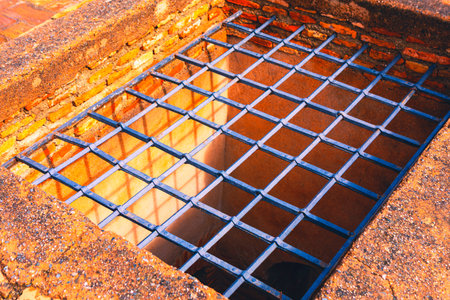 Metal grate covers a brick opening in the ground, suggesting a hidden underground space. Weathered...