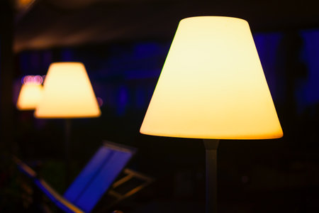 Row of illuminated lamps with conical shades, creating a warm and inviting atmosphere. Background is dark with a hint of blue light, making the glowing lamps stand out prominentlyの写真素材