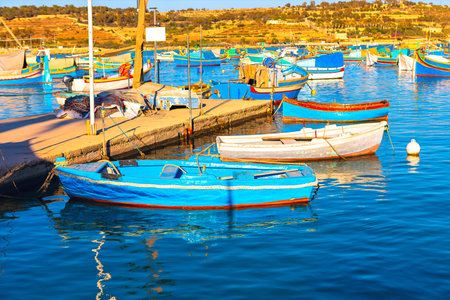 Serene harbor scene with numerous small boats, many painted in bright colors, docked along a wooden pier. In background, a hilly landscape with sparse vegetation stretches under a clear skyの写真素材
