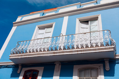 Blue building with a white balcony railing that has intricate designs, set against blue sky. Classic architecture with a striking blue facade and a detailed white balconyの写真素材