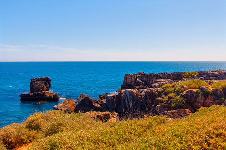 Rugged coastal landscape with dramatic cliffs and rocky formations extending into blue ocean....