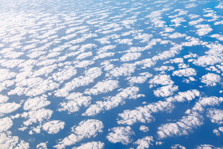 View of a vast expanse of cumulus clouds, scattered across a vibrant sky. Densely packed cumulus...