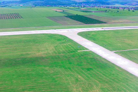 Airfield with intersecting concrete runways surrounded by green fields. Visible from above, the runway cuts a bold geometric path through the landscapeの写真素材