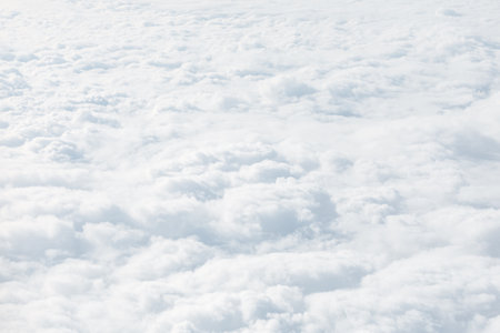 Aerial view of dense, fluffy white clouds forming a soft, layered expanse. Tranquil scene suggests...