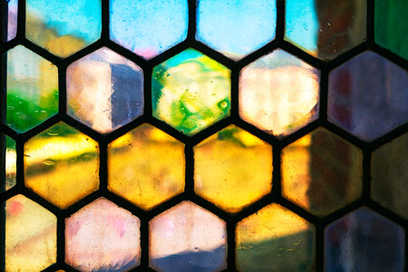 Vibrant hexagonal stained glass creates a colorful mosaic effect, blending shades of yellow, blue, green and pink. Light passing through textured glass evokes artistic, abstract and decorative charmの写真素材