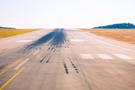 Runway with numerous tire skid marks, indicating frequent landings and takeoffs. Runway is surrounded by grassy areas and hills in backgroundの写真素材