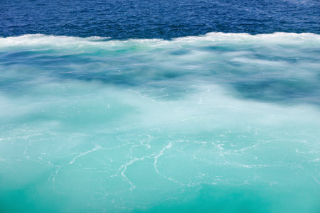 Ocean with a striking contrast between turquoise and deep blue water, separated by a foamy, white line. Lighter water in the foreground appears cloudy with visible white streaks and patternsの写真素材