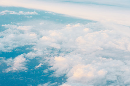 Aerial shot looking down at a vast expanse of clouds. Clouds appear fluffy and white, with some casting soft shadows on the blue sky belowの写真素材