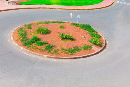 Roundabout featuring a central planting bed with sparse vegetation and road signs. Circular traffic...