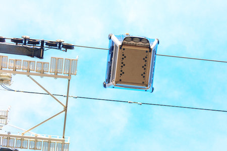 Cable car suspended from wires, viewed from below against a blue sky. Image emphasizes the bottom...