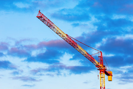 Tower crane set against a vibrant blue sky filled with scattered clouds. Construction machinery...