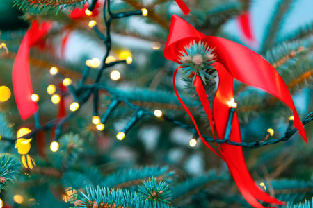 Christmas tree shows glowing yellow lights wrapped around green pine needles. Red ribbon adds festive charm, evoking warmth and tradition in a cozy holiday settingの写真素材