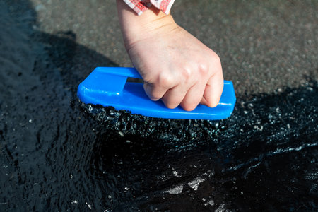 Hand pushes brush through thick black sealant, applying waterproof coating to surface like roof or pavement. Process involves using asphalt or tar compound with mastic brush for sealing and repairingの写真素材