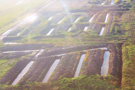 Aerial view of parallel trenches dug into an earthy, grassy landscape. Deep land cuts are partially filled with water and appear to be part of an excavation or agricultural process for irrigationの写真素材
