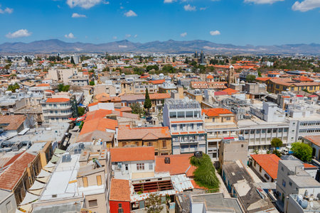 Aerial panorama of Nicosia, Cyprus, showcasing dense urban architecture with traditional tiled roofs under blue sky. In background distinctive profile of Kyrenia Mountains frames horizonの写真素材