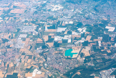 Aerial view of patchwork farmland and urban neighborhoods beside a turquoise lake. Winding roads...