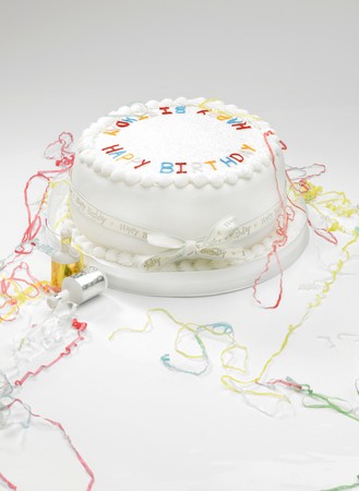 A white birthday cake with streamers on a white surface.の写真素材