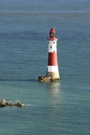 A red and white lighthouse surrounded with calm water during daytimeの写真素材