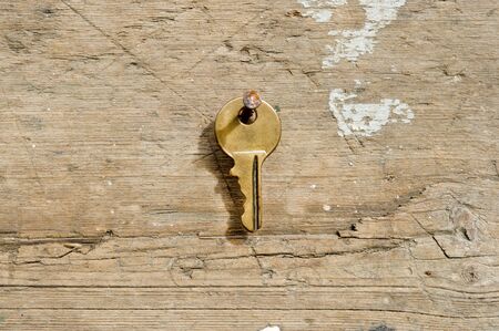 a single bronze key hanging on a rusty nail on piece of woodの写真素材