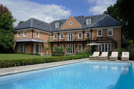 the rear garden of a large detached house and swimming pool with lounge chairsのeditorial素材