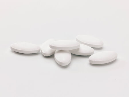 a pile of white lozenge shaped pills on a white backgroundの写真素材