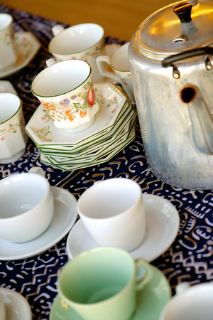 Stacks of china tea cups and saucers and a metal kettleの写真素材