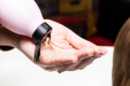 The hairdresser pours a transparent shampoo from a jar into the palm of his hand to apply it on the...