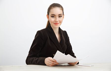 Girl in dark jacket holding a stack of documents. She is sitting at the office table against a white background.の写真素材