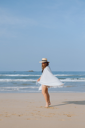 Girl in a hat and a plaid walks along the beach on the ocean shoreの写真素材